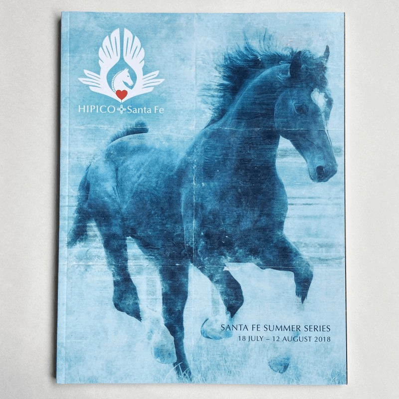 Magazine cover with a blue toned horse galloping and logo for an equestrian event