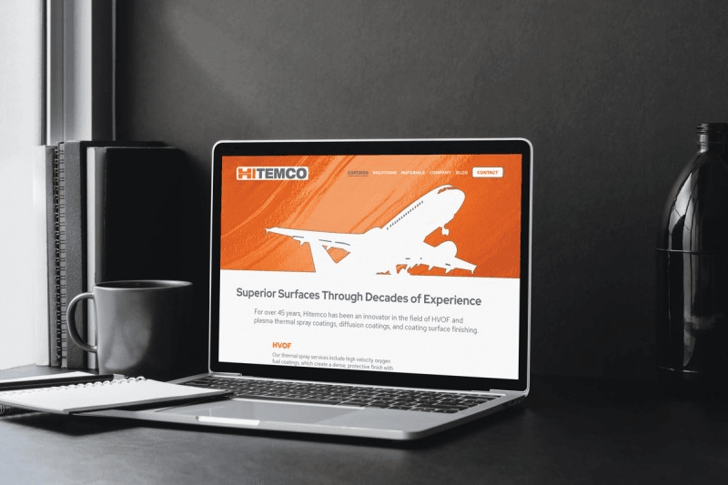Hitemco website home page displayed on laptop in modern gray interior room with daylight